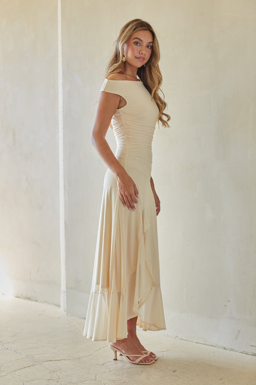 Woman wearing a long off-shoulder cream dress against a white background
