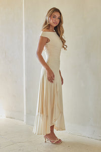 Woman wearing a long off-shoulder cream dress against a white background