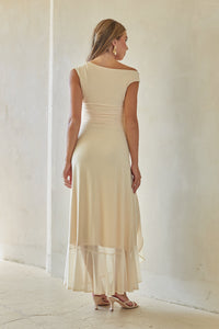 Woman wearing a beige dress standing against a white wall.