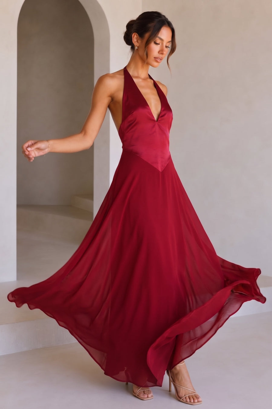A model wearing a red halter-neck maxi dress with a deep V-neckline, standing against a studio background.