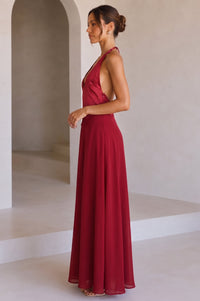 A model wearing a red halter-neck maxi dress with a deep V-neckline, standing against a studio background.