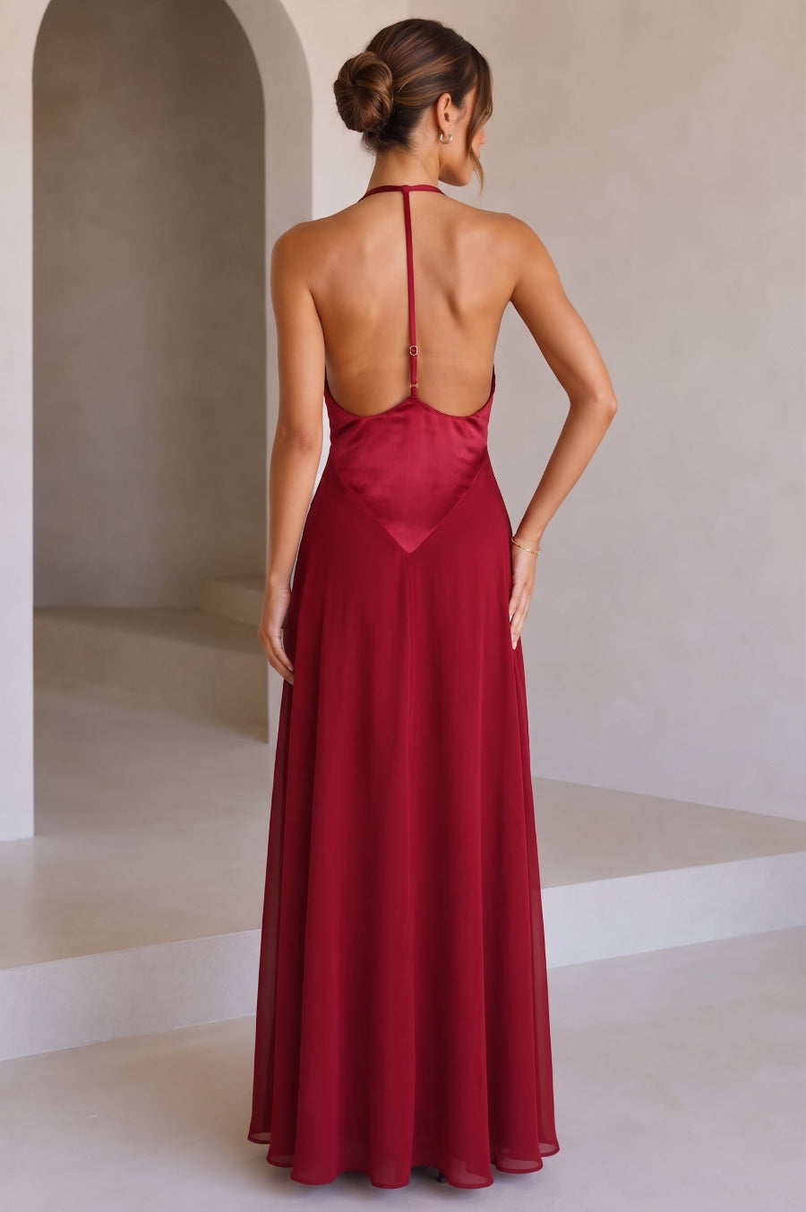 A model wearing a red backless maxi dress with a t-back, standing against a studio background.