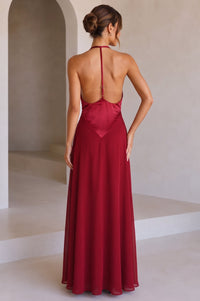 A model wearing a red backless maxi dress with a t-back, standing against a studio background.