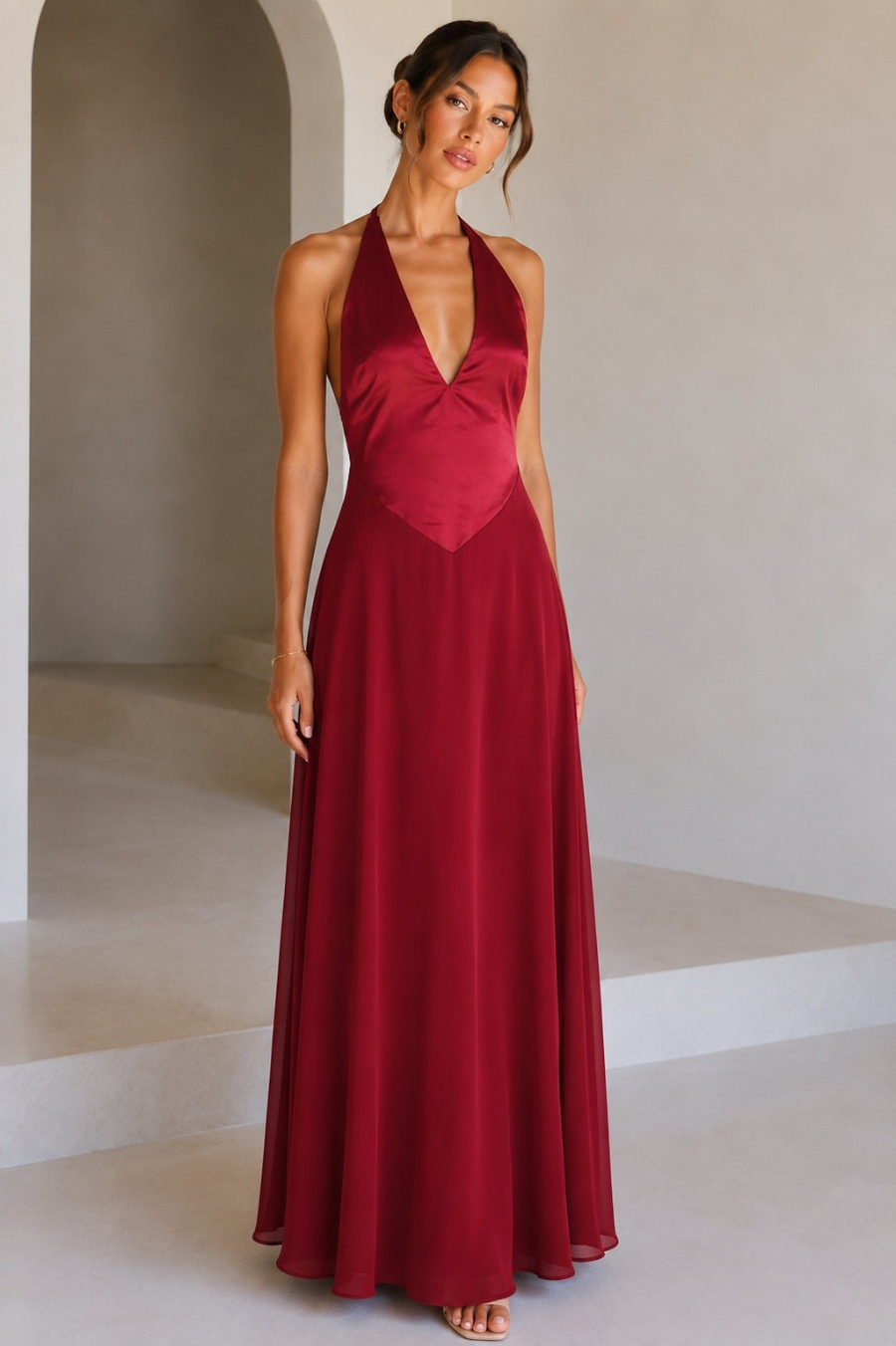 red-image | A model wearing a red halter-neck maxi dress with a deep V-neckline, standing against a studio background.