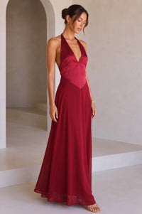 A model wearing a red halter-neck maxi dress with a deep V-neckline, standing against a studio background.