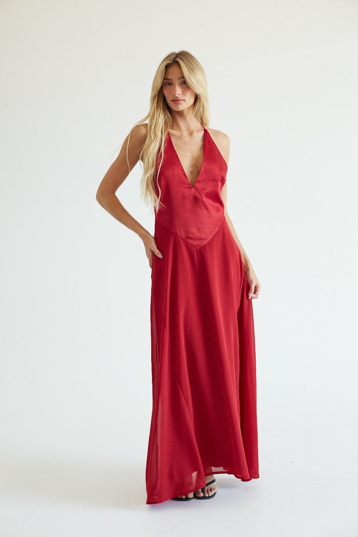 red-image | A blonde model wearing a red halter-neck maxi dress with a deep V-neckline, standing against a plain white studio background.