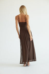 A woman wearing a dark brown pleated maxi dress with thin spaghetti straps, shown from the back against a plain white studio background.