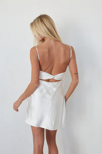 Woman wearing a white satin nightgown with thin straps on a plain background