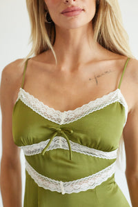 A close-up of a woman wearing an olive green camisole top with white lace trim and thin shoulder straps.