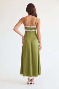 A woman shown from the back wearing a sleeveless olive green maxi dress with thin straps, a lace-trimmed back bodice, and a white lace hem, photographed against a plain light background.
