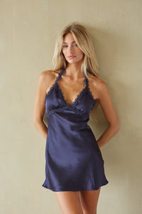 Woman wearing a navy satin dress against a beige wall