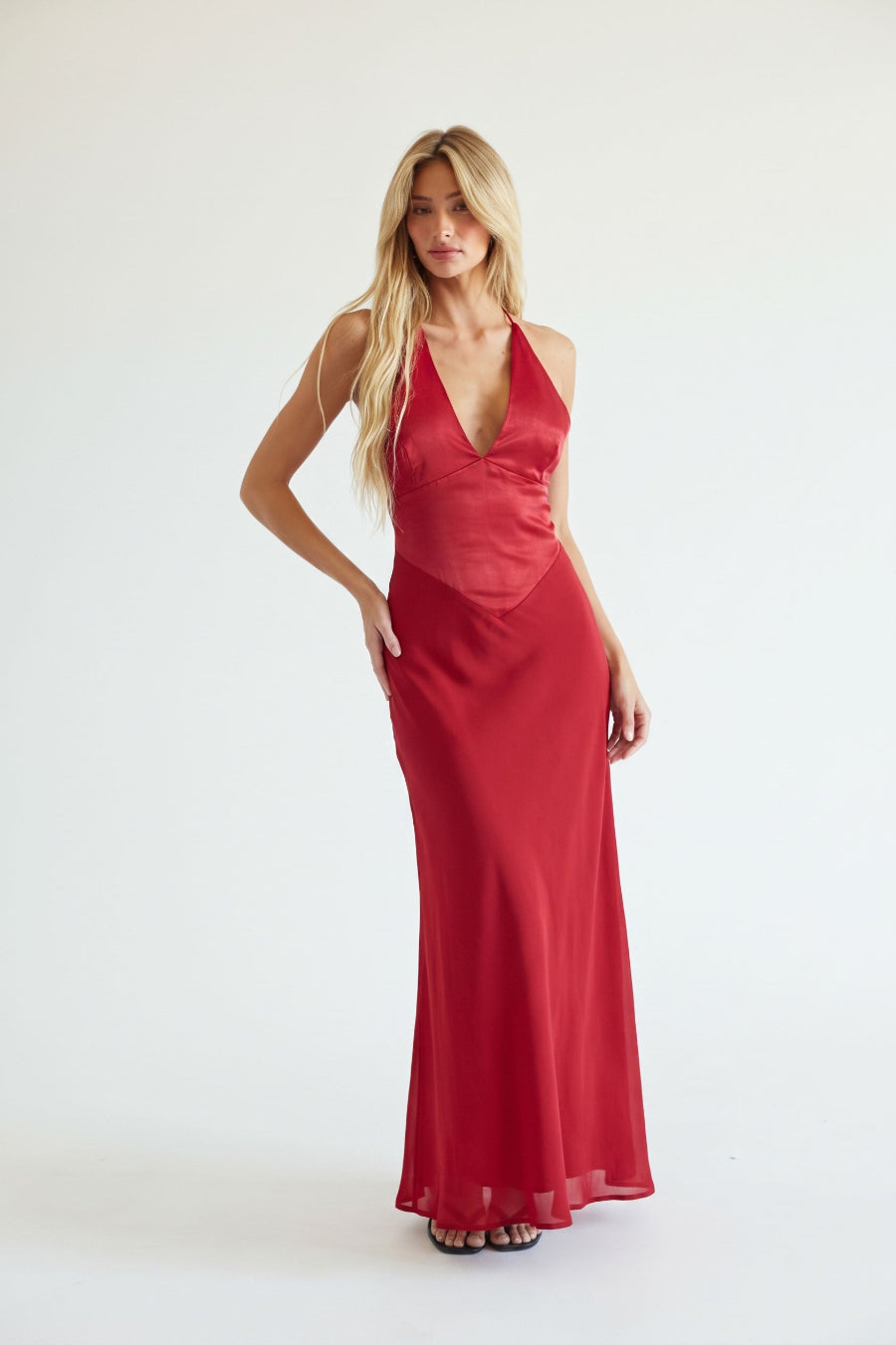 red-image | A model wearing a red halter-neck maxi dress with a deep V-neckline, standing against a white background.