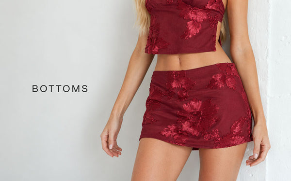 A model wearing a matching burgundy two-piece set with a floral jacquard pattern, featuring a crop top and a high-waisted mini skirt, set against a light gray wall with the text 'BOTTOMS' on the left.
