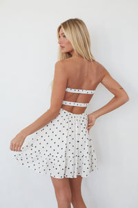 Woman wearing a white polka dot dress with a backless design on a plain background
