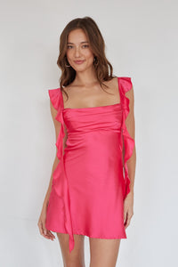 Woman wearing a pink dress with ruffled straps against a white background