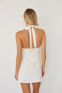 Woman wearing a white halter neck dress on a plain background