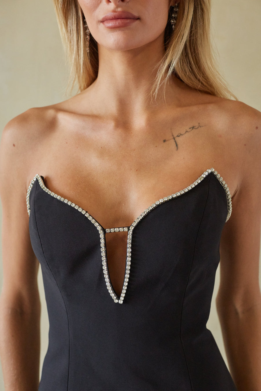 A close-up of a model wearing a strapless black dress with a sweetheart neckline and crystal embellishments along the edges and center cutout.