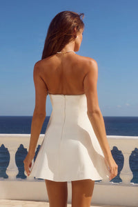Woman in a white dress standing on a balcony with a blue ocean view