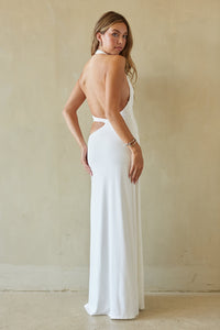 Woman wearing a white dress with an open back against a beige wall.