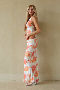 Woman wearing a floral dress standing against a beige wall.