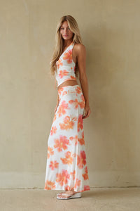 Woman wearing a floral two-piece outfit against a beige wall.