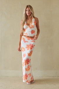 Woman wearing a floral two-piece outfit against a beige wall.