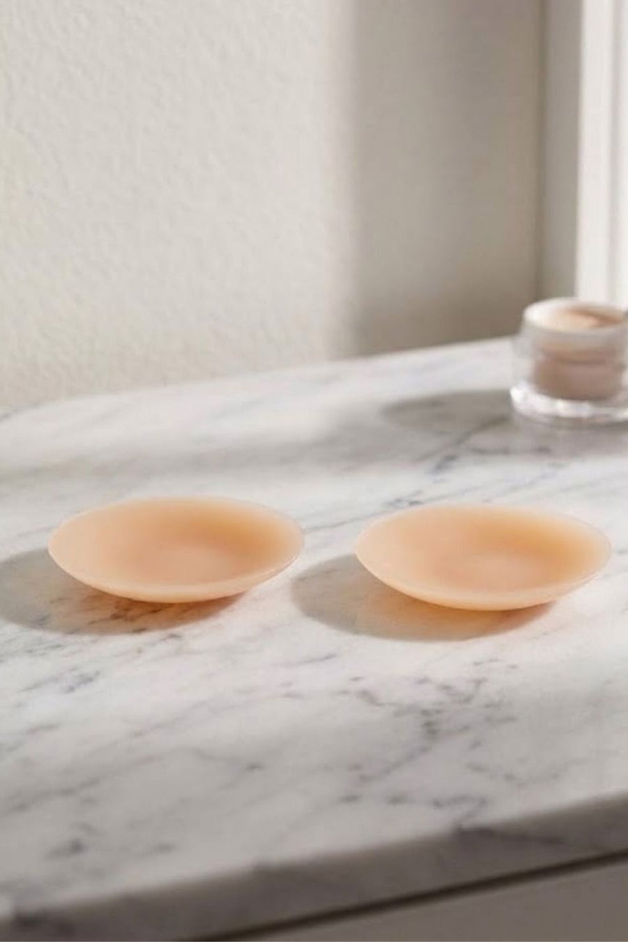 Two peach-colored silicone breast implants displayed on a white marble countertop with a soft-focus background.