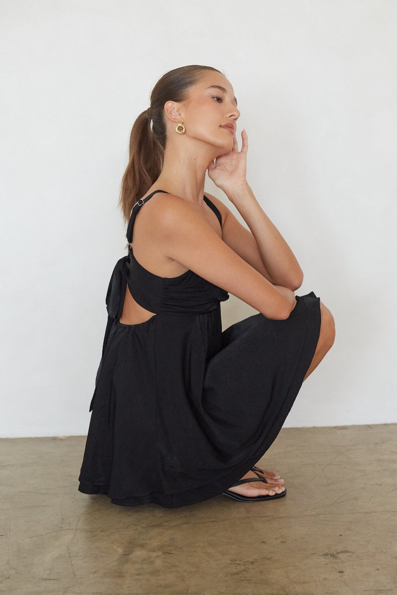 black-image | Woman in a black dress sitting on the floor against a white wall.