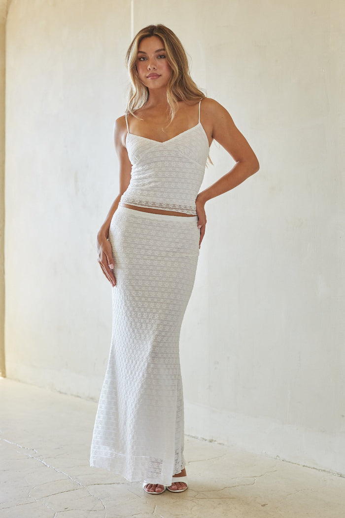 Woman wearing a white textured top and skirt set against a plain background