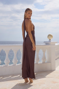 Woman in a brown dress standing on a balcony with ocean view