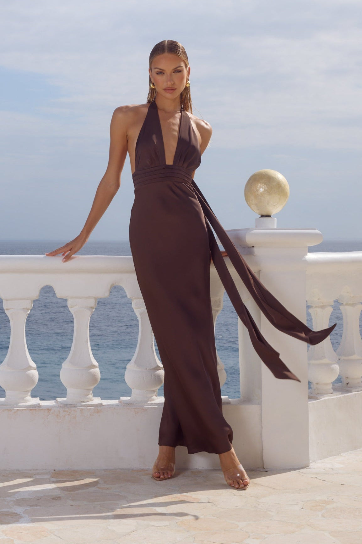 brown-image | Woman in a brown halter neck jumpsuit standing on a balcony with ocean view