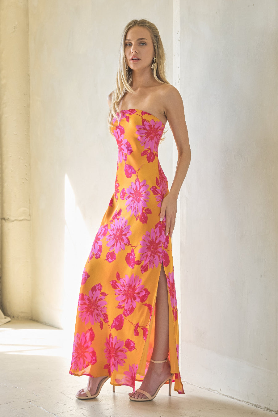 Woman wearing a strapless floral dress with pink and yellow flowers in a bright room.