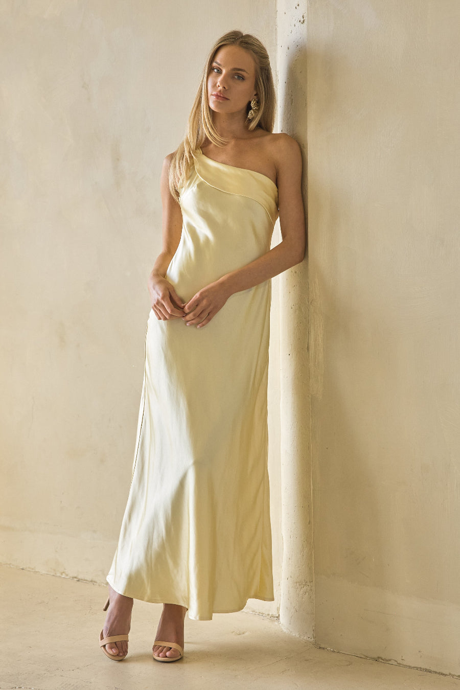 yellow-image | Woman in a light yellow one-shoulder dress standing against a plain wall.
