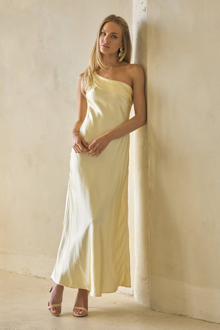 yellow-image | Woman in a light yellow one-shoulder dress standing against a plain wall.