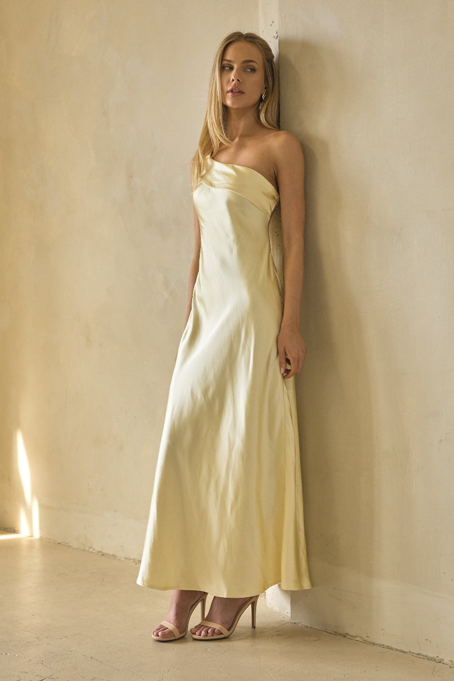 Woman in a light yellow strapless dress standing against a plain wall.