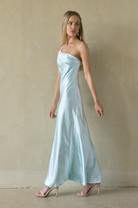 Woman wearing a light blue satin dress against a beige wall.