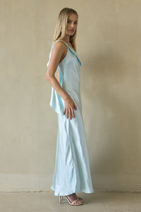 Woman wearing a light blue dress standing against a beige wall.