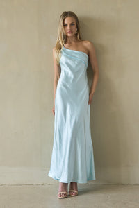 blue-image | Woman wearing a light blue one-shoulder dress against a beige wall.