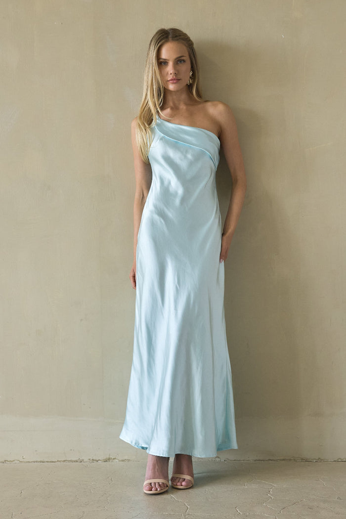 blue-image | Woman wearing a light blue one-shoulder dress against a beige wall.