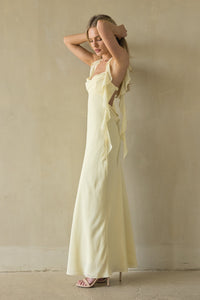 Woman wearing a light yellow slip dress against a beige wall.