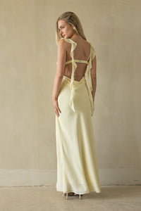 Woman wearing a light yellow dress with cut-out back in a minimalistic setting