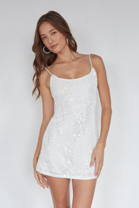 Woman wearing a white sequin dress against a plain background