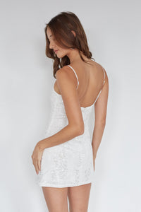 Woman wearing a white lace dress with thin straps on a plain background