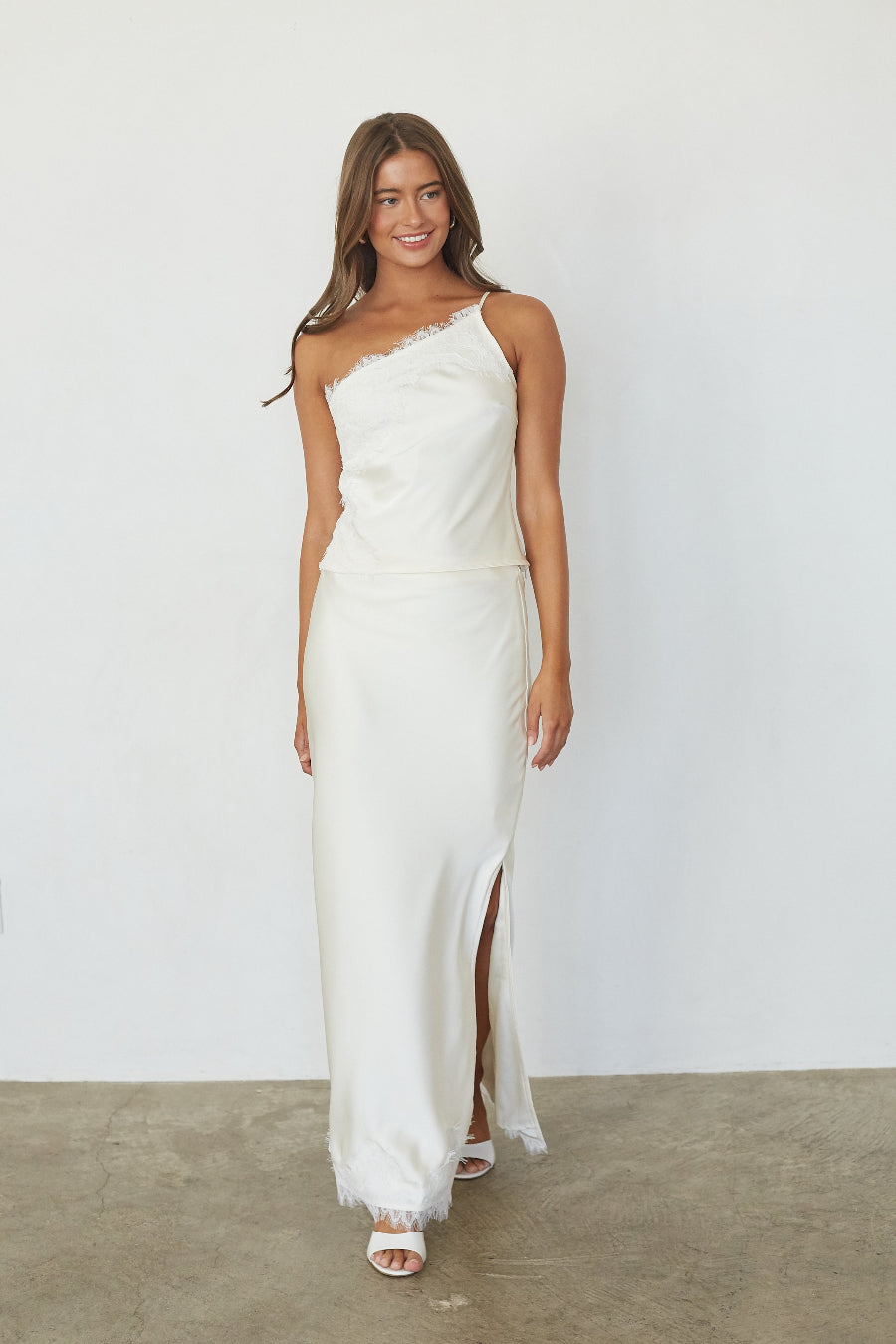 white-image | brunette model wearing a white lace trim asymmetrical top and satin skirt front image