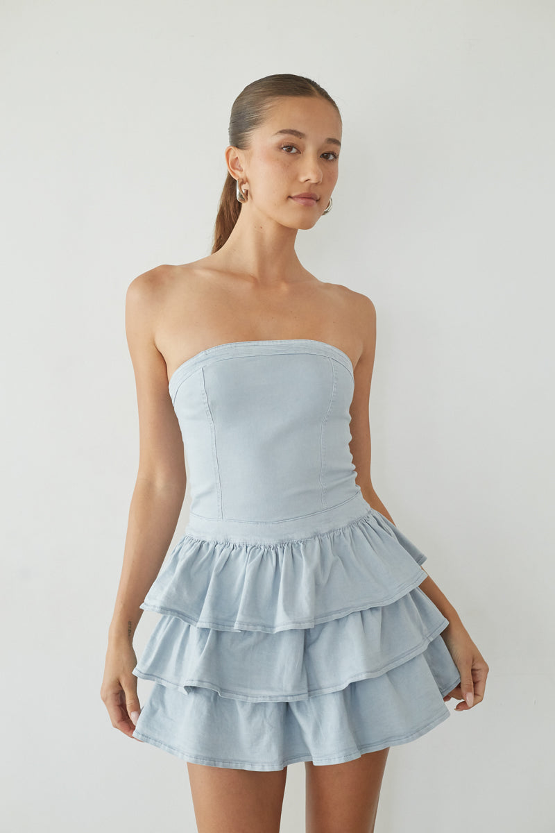 blue-image | Woman wearing a light blue strapless dress with ruffled layers on a plain background