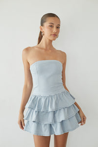 blue-image | Woman wearing a light blue strapless dress with ruffled layers on a plain background