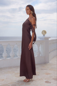 Woman in a brown dress standing on a balcony with ocean view