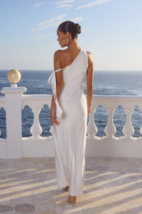 Woman in a white one-shoulder dress standing on a balcony with ocean view