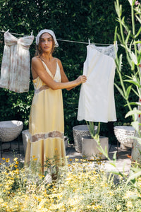 Woman hanging clothes on a line outdoors with greenery and flowers in the foreground