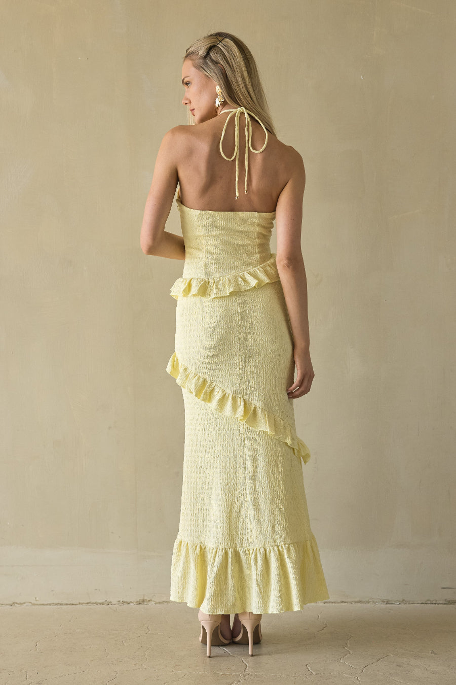 Woman wearing a yellow strapless dress with ruffled details against a beige background